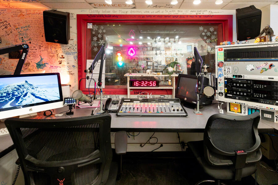 Audio console and a view through the broadcast studio glass wall into the lounge