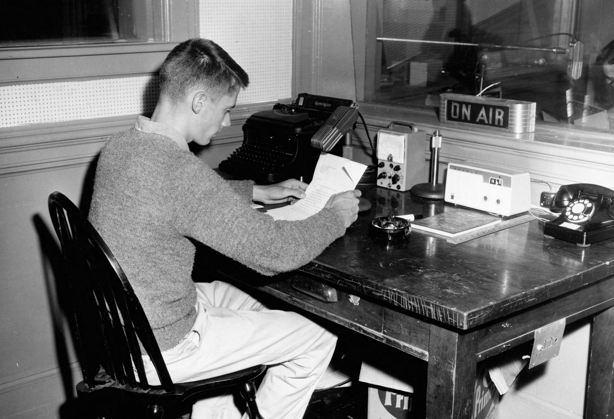 Student at radio station reading a piece of paper.