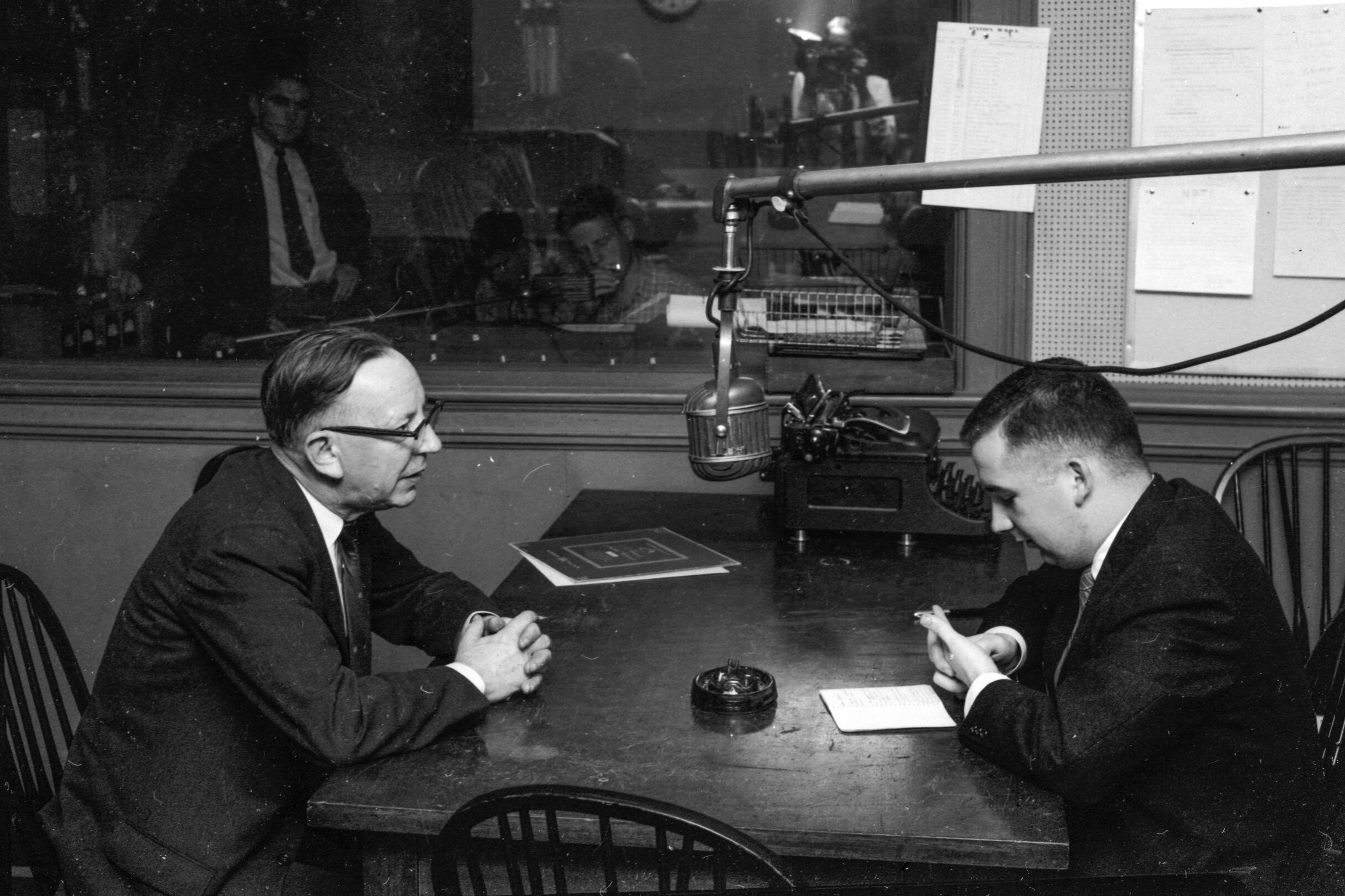 A student and an adult sitting at a table for a radio interview.