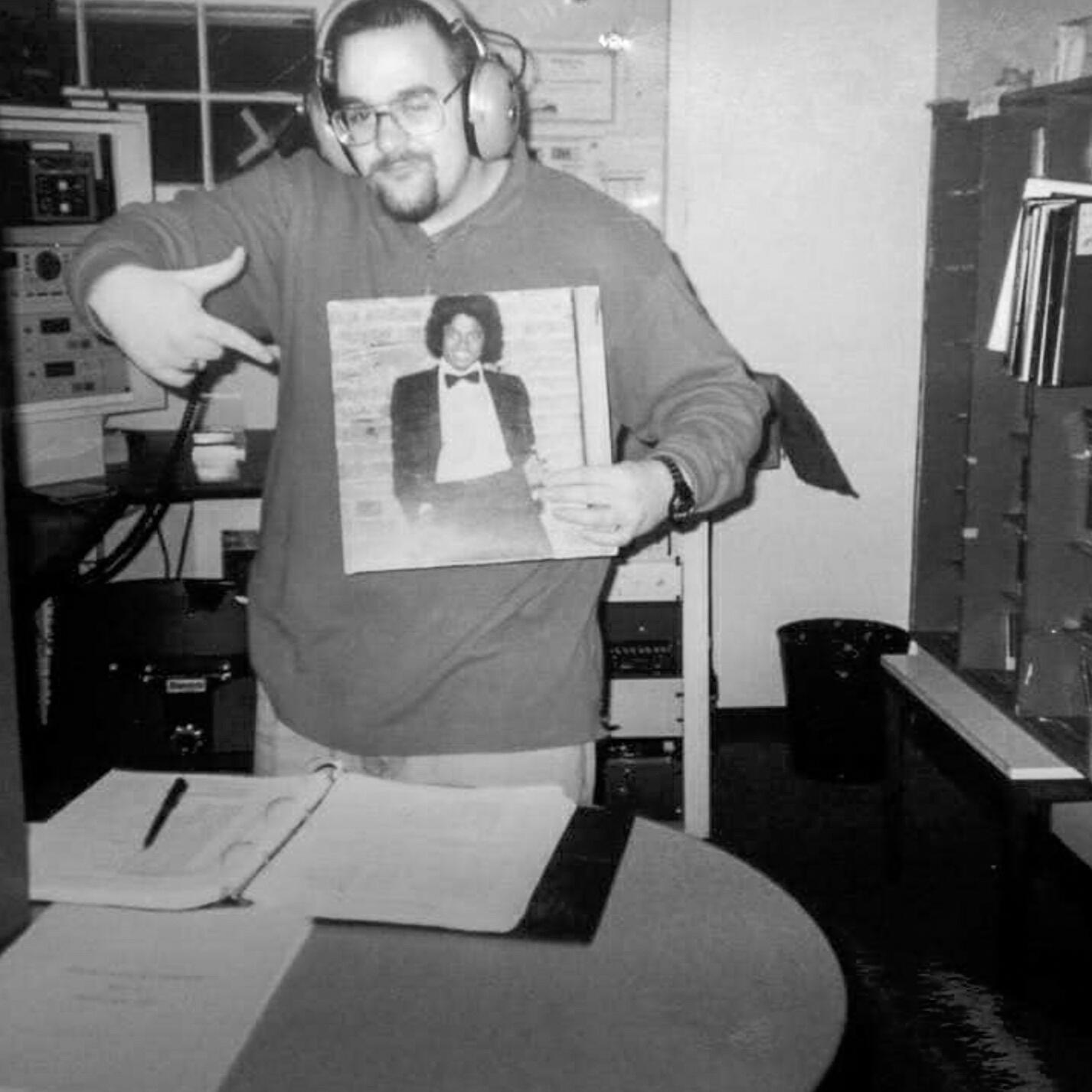 A DJ with headphones on holds a Michael Jackson record and points at it
